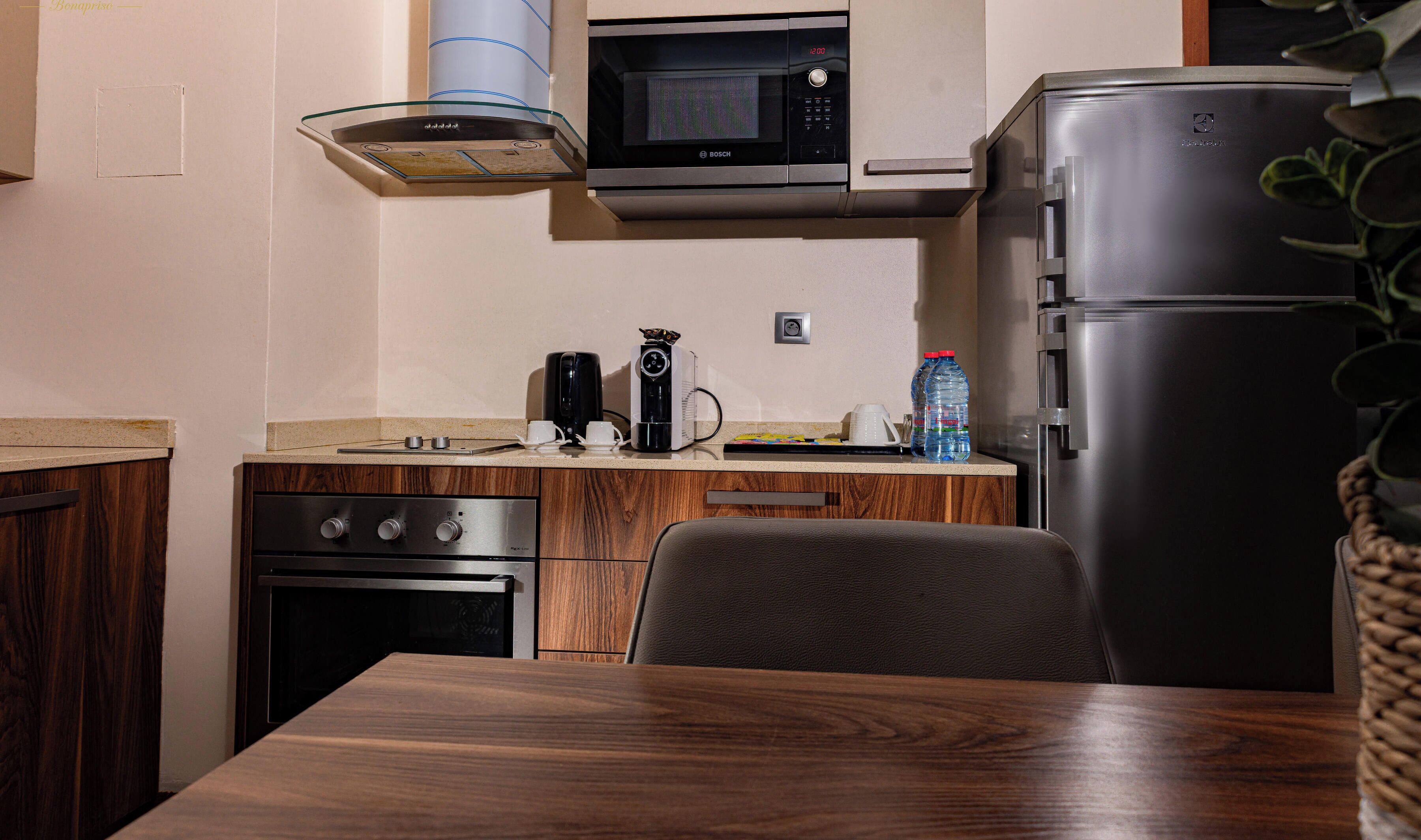 Une cuisine compacte équipée d’un four à micro-ondes Bosch, d’une machine à café, d’un réfrigérateur et d’une table en bois.