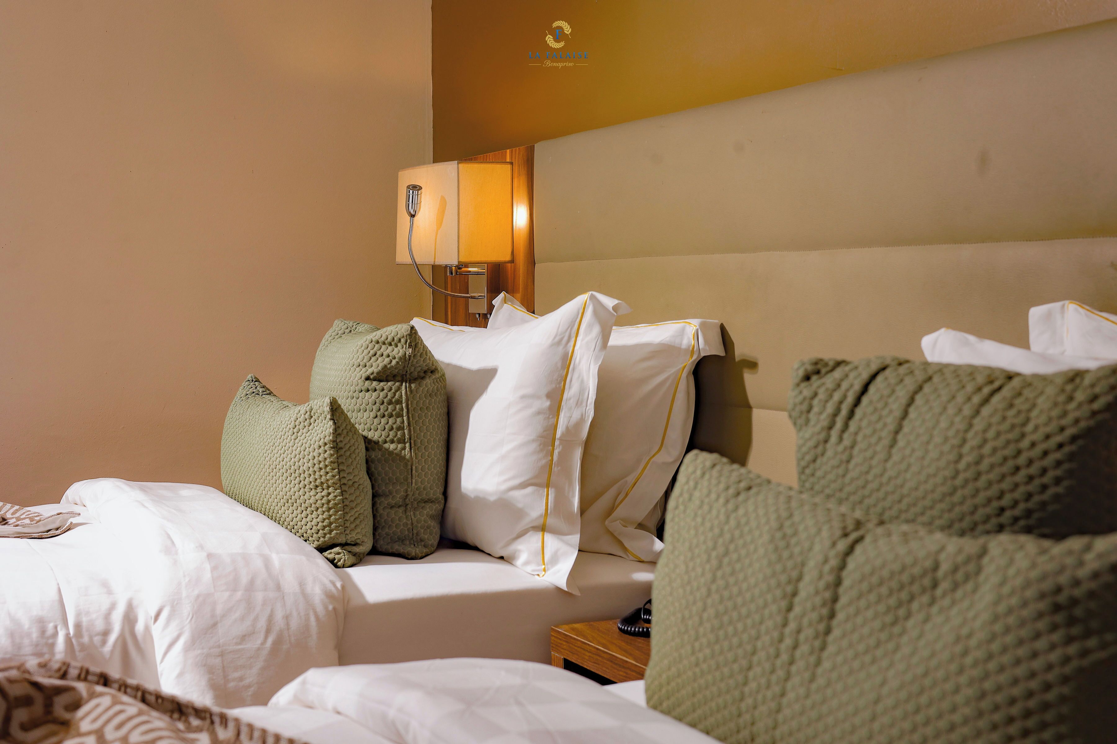 Una habitación de hotel con cama, almohadas, mesita de noche y lámpara.