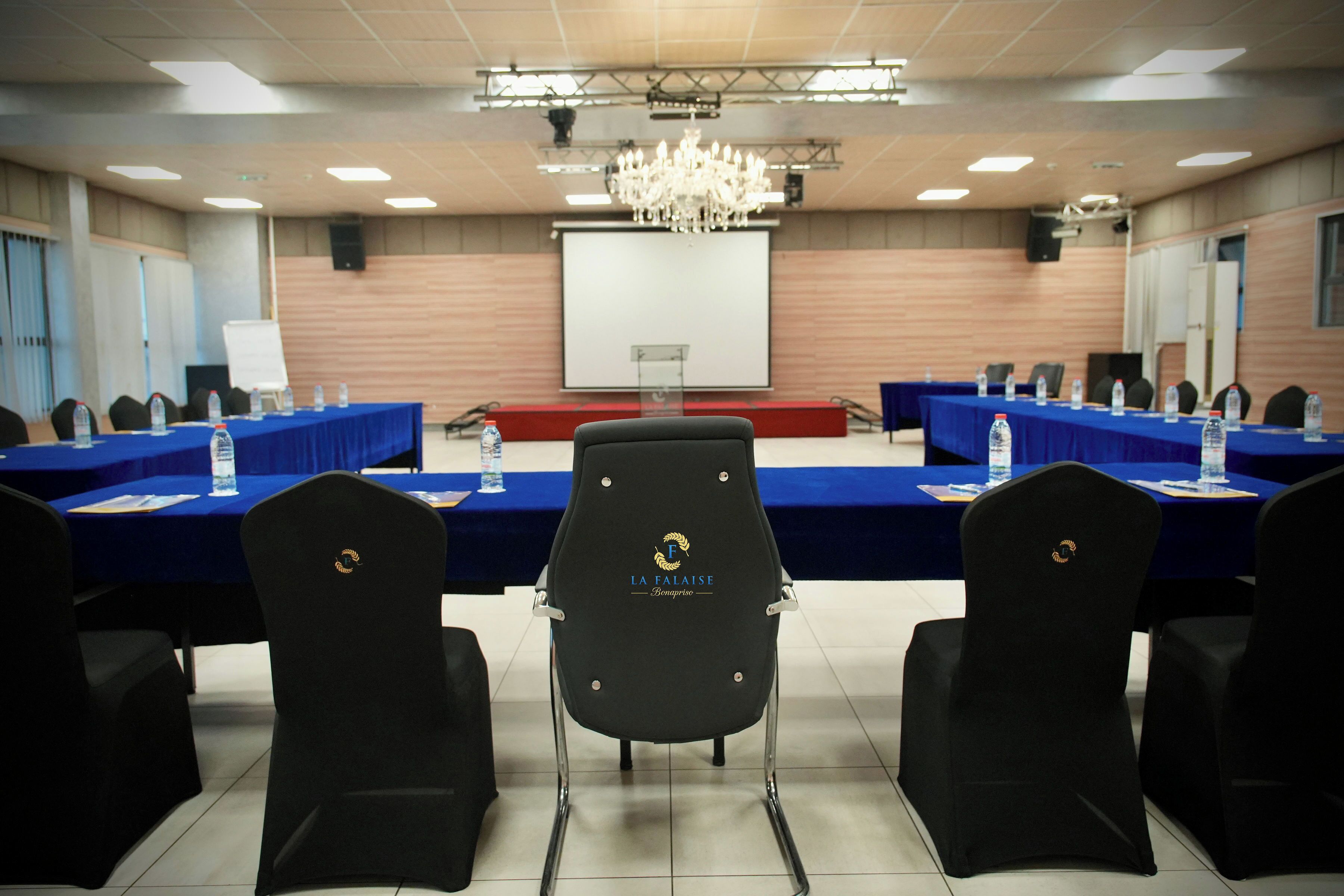 A conference room with a long table, chairs, a projector screen, and a chandelier.