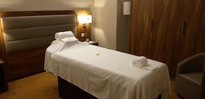 Ein Hotelzimmer mit einem Bett, einem Nachttisch, einer Lampe, einem Holzschrank und einem Sessel.