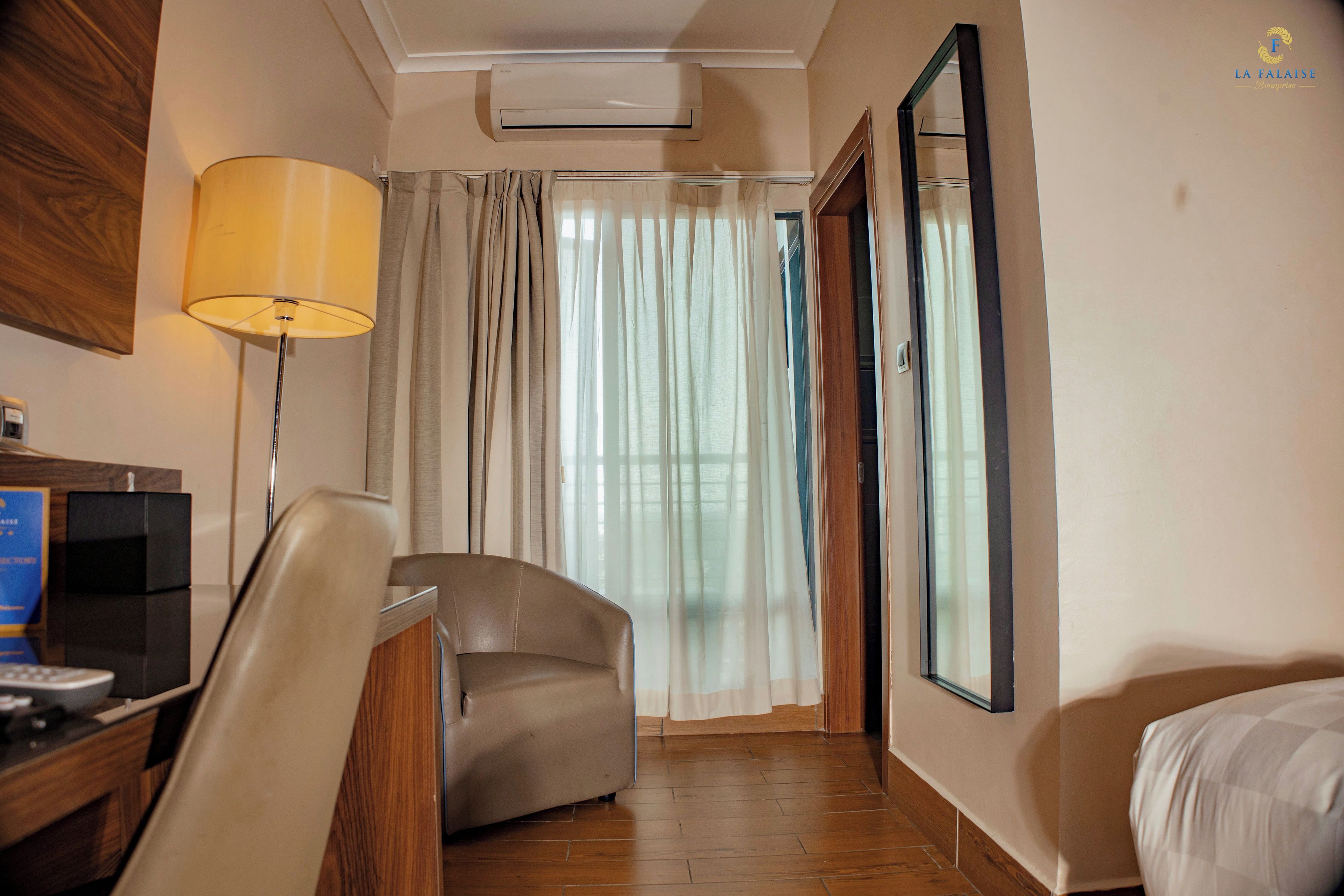 A hotel room with a desk, chair, bed, and a large mirror.