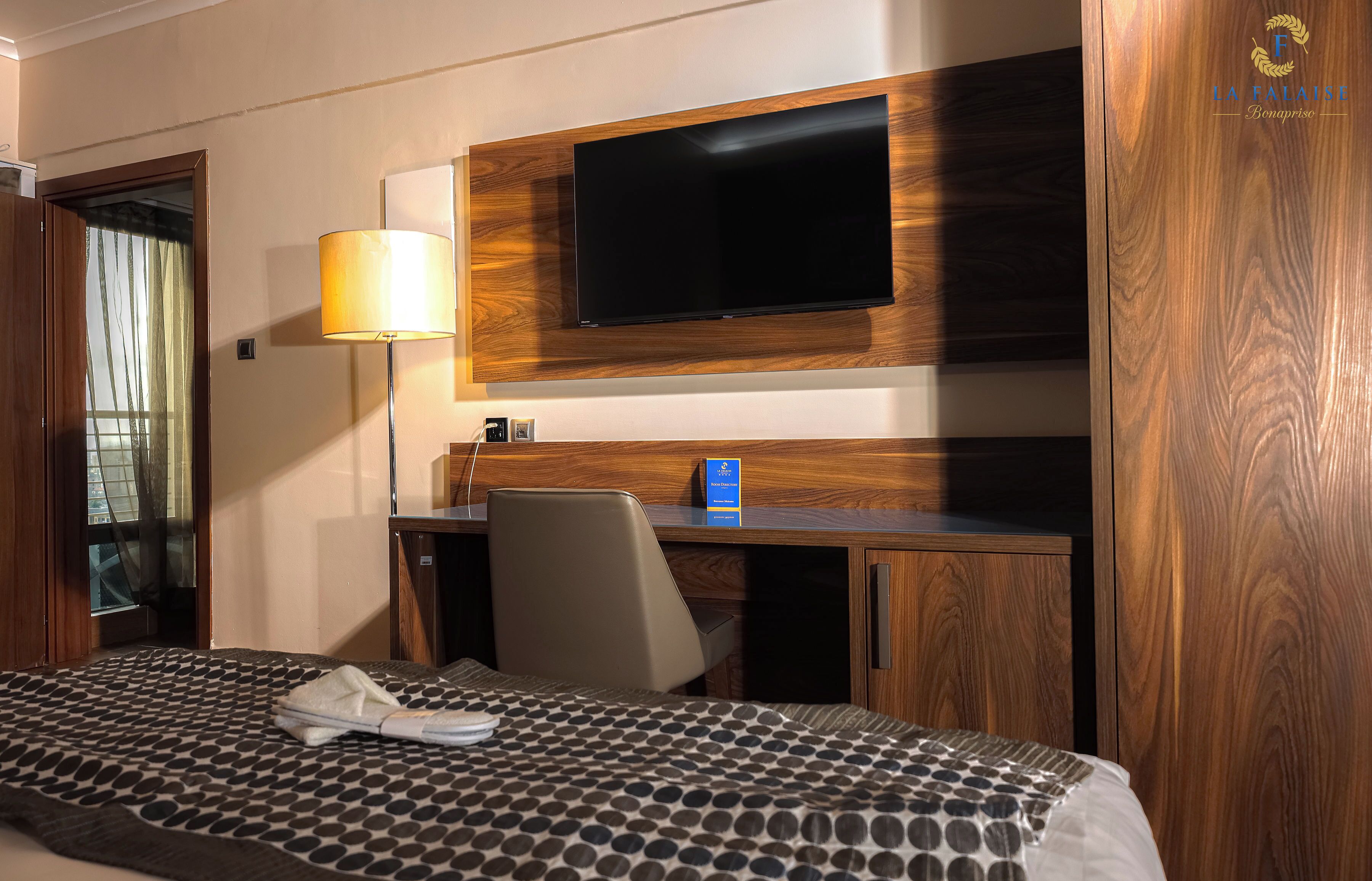 Habitación de hotel con cama, escritorio, silla, televisor montado en la pared y lámpara.