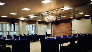 A conference room with multiple tables, chairs, a projector screen, and a chandelier.