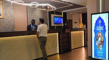 Un espace d’accueil d’hôtel au design moderne, comprenant un comptoir d’accueil, un écran de télévision et un panneau d’affichage numérique faisant la publicité d’un restaurant.