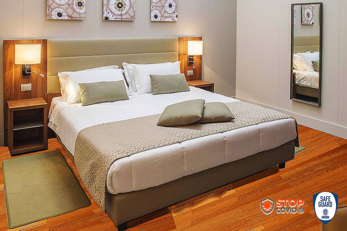 A neatly arranged hotel room with a large bed, two bedside tables with lamps, a bedside mirror, and decorative wall art.