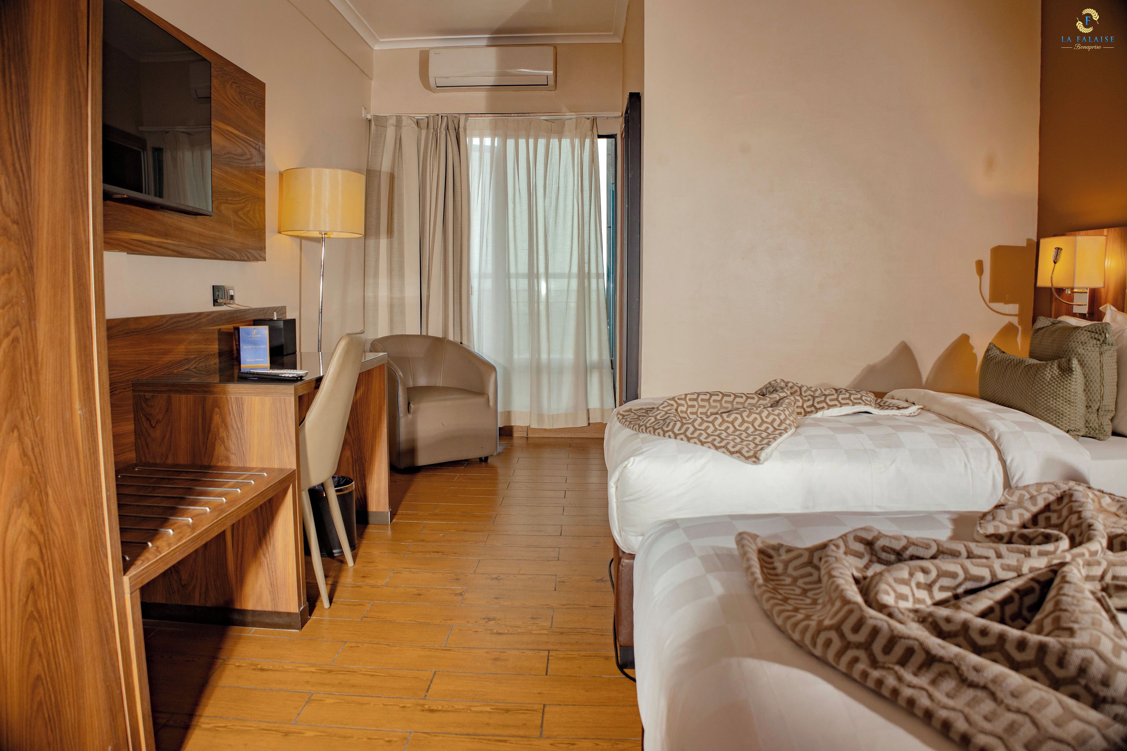 A hotel room with a bed, a desk, a chair, a TV, and a window with curtains.