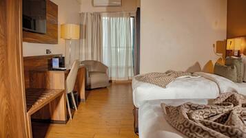 A hotel room with a bed, a desk, a chair, a TV, and a window with curtains.