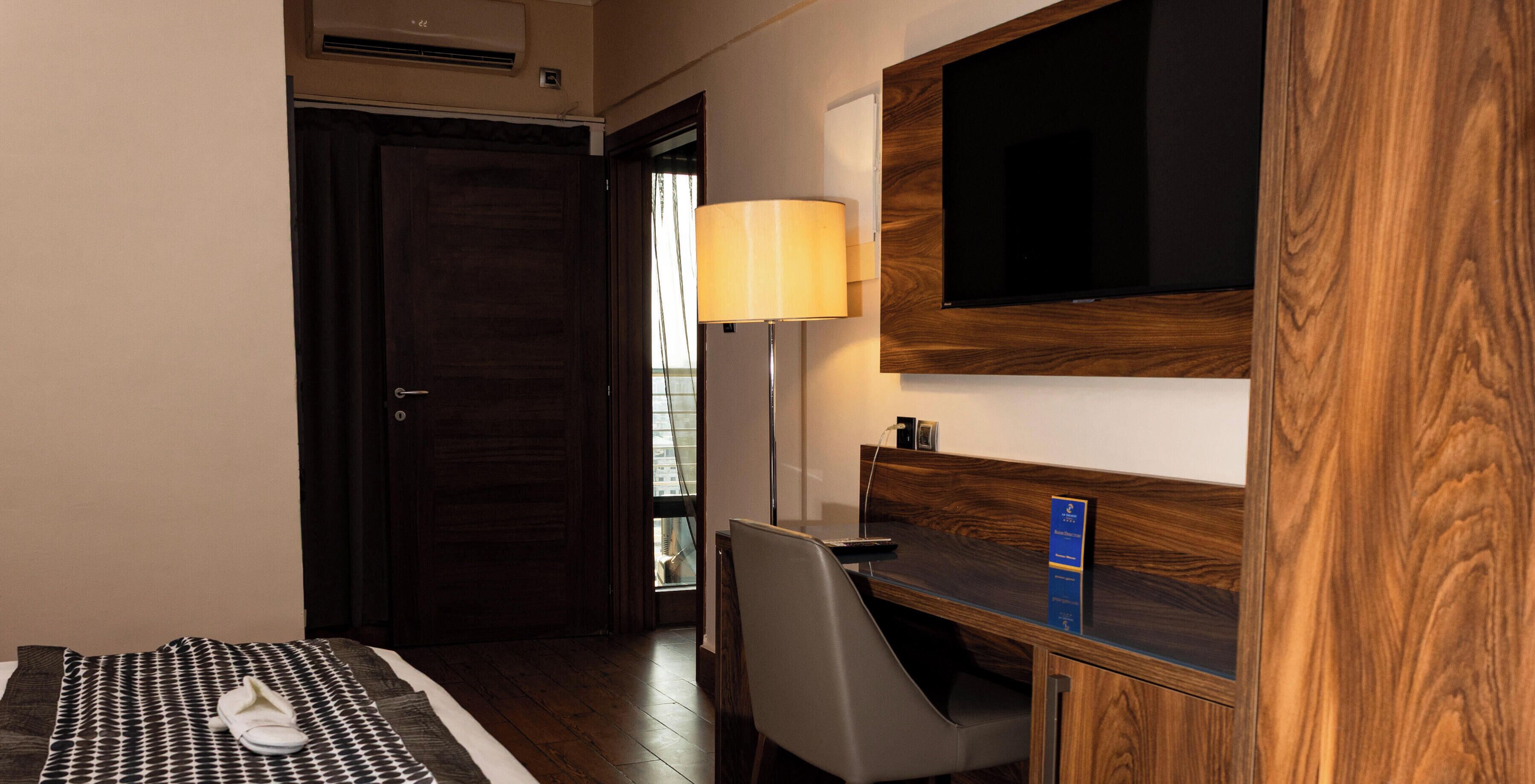 A hotel room with a bed, a desk, a chair, a TV, and a lamp.