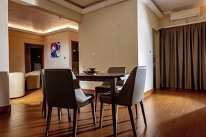 A dining area with a wooden table and four chairs, a painting on the wall, and an air conditioning unit. - Hotel La Falaise Bonapriso (Douala)