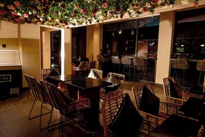 A dining area with a black table and wicker chairs, surrounded by walls with large windows. - Hotel La Falaise Bonapriso (Douala)