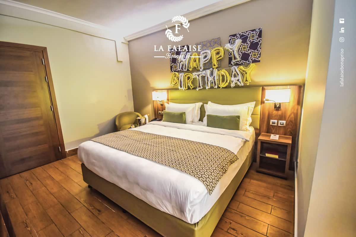A hotel room with a bed, two bedside tables, a nightstand, a wall decoration, and a door.