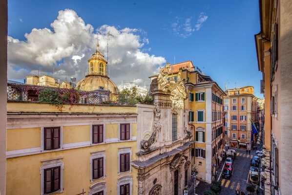 Vista callejera con edificios históricos, una cúpula destacada y una estatua.