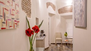 A modern hallway with a glass table holding red flowers, a white door, and a seating area with a chair and table. - MySuite Tower Pantheon (Rome)