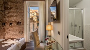 A hotel room with a brick wall, a bed, a glass table with a lamp, a chair, and a shower area. - MySuite Tower Pantheon (Rome)