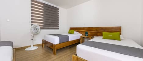 A hotel room with two beds, a standing fan, and a window with blinds.