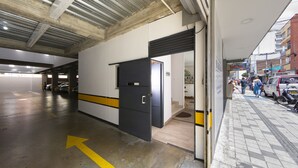A parking garage with directional arrows on the floor, a door leading to a corridor, and a street with pedestrians and parked vehicles outside. - Ayenda Marckia 1901 (Armenia)