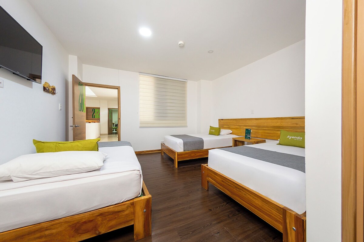 Ein Hotelzimmer mit zwei Holzbettgestellen, einem Flachbildfernseher und einer Tür zu einem Badezimmer.