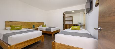 A hotel room with two wooden beds, each with a white mattress, grey bedspread, and a green pillow labeled "Ayenda".