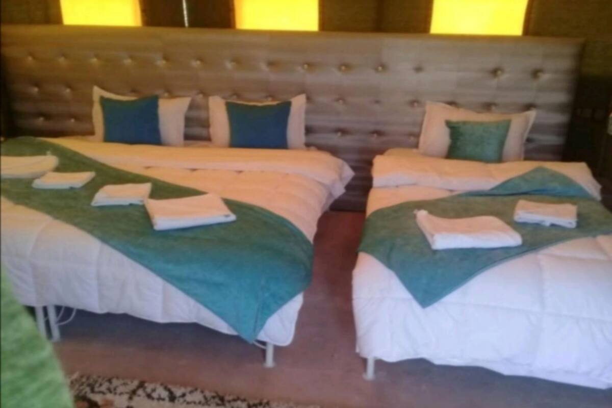 A hotel room with two beds, each with neatly folded towels and green throw blankets.