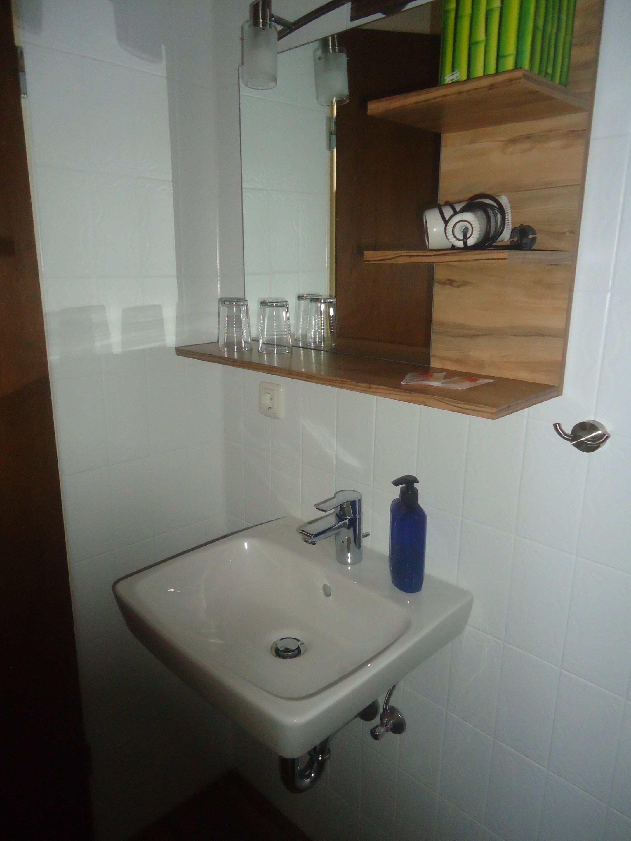 Une salle de bain avec un lavabo blanc, un miroir et une étagère en bois au-dessus du lavabo.
