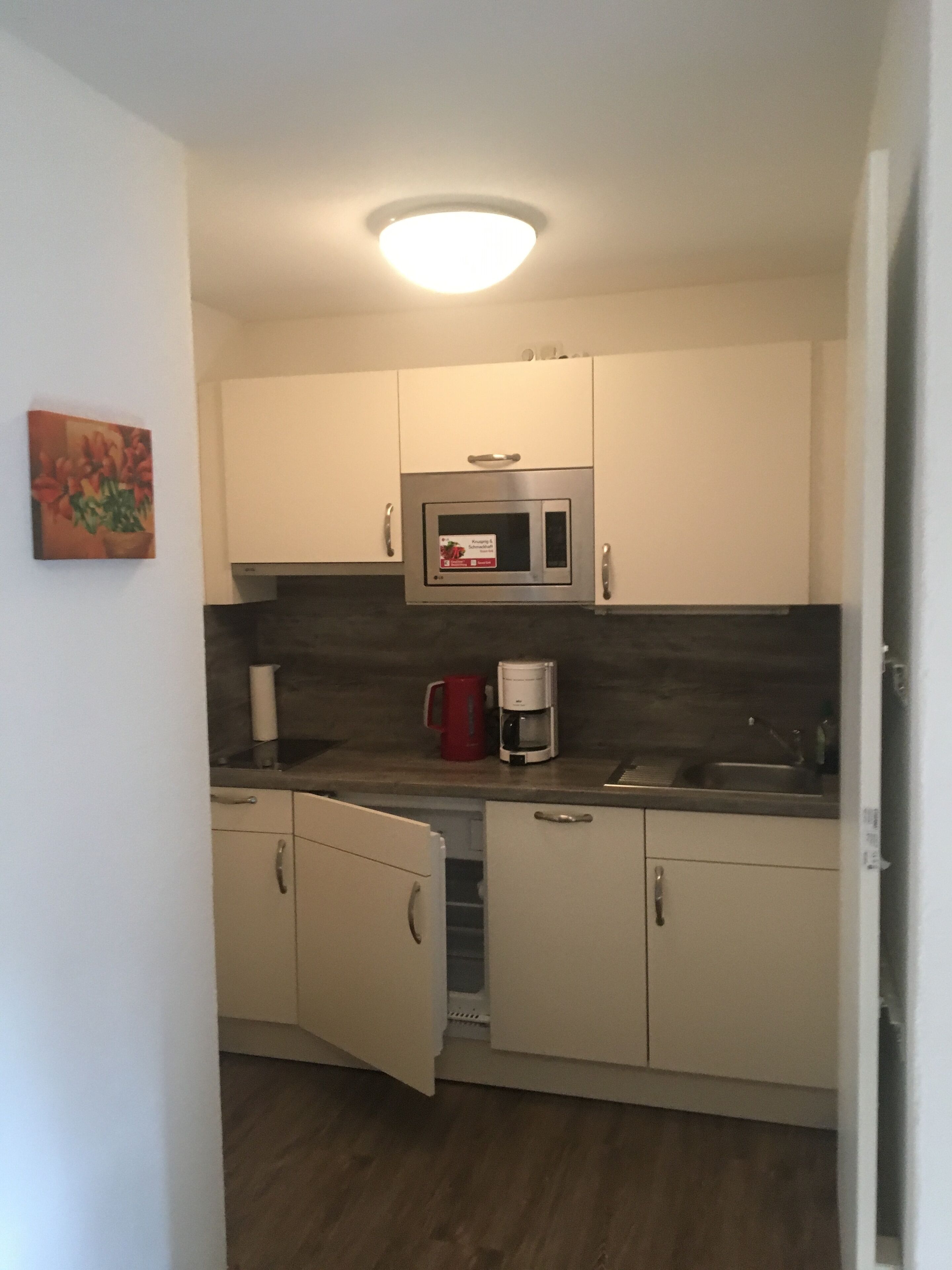 A compact kitchen with white cabinets, a microwave, a coffee maker, and a sink.