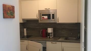 A compact kitchen with white cabinets, a microwave, a coffee maker, and a sink.
