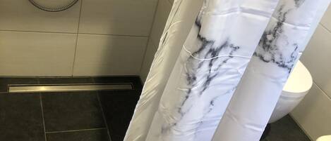 A bathroom with a shower, a toilet, and a marble-patterned shower curtain.