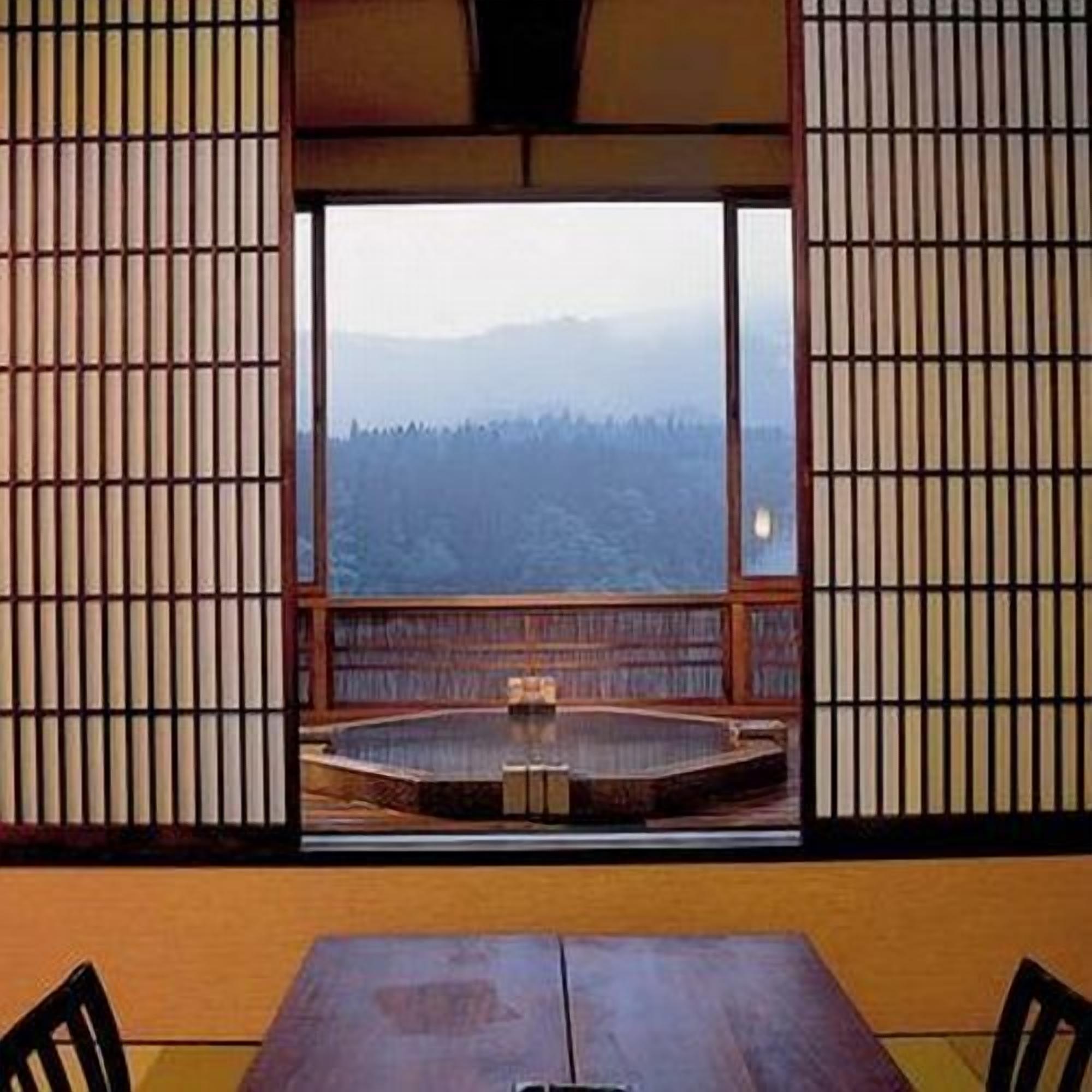 Une pièce avec une table et des chaises en bois, une vue sur une forêt par une grande fenêtre et une porte coulissante traditionnelle japonaise.