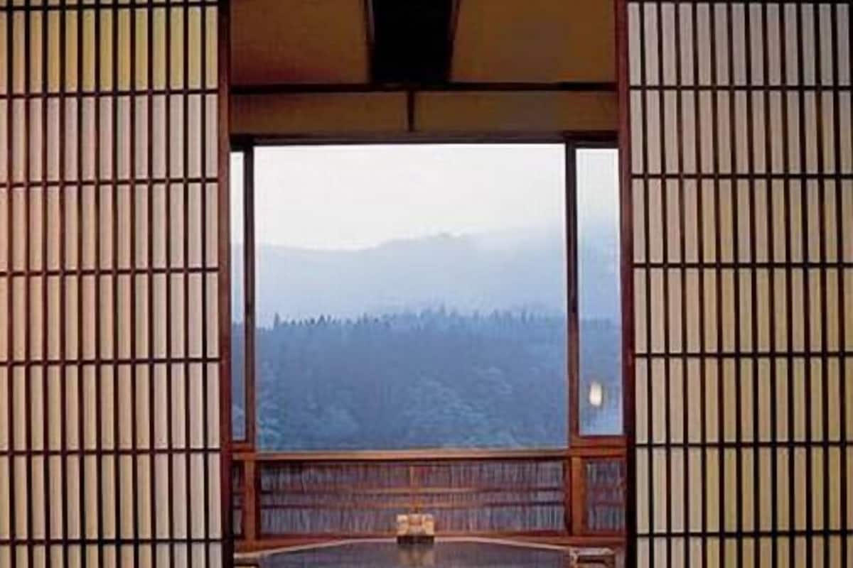Une pièce avec une table et des chaises en bois, une vue sur une forêt par une grande fenêtre et une porte coulissante traditionnelle japonaise.