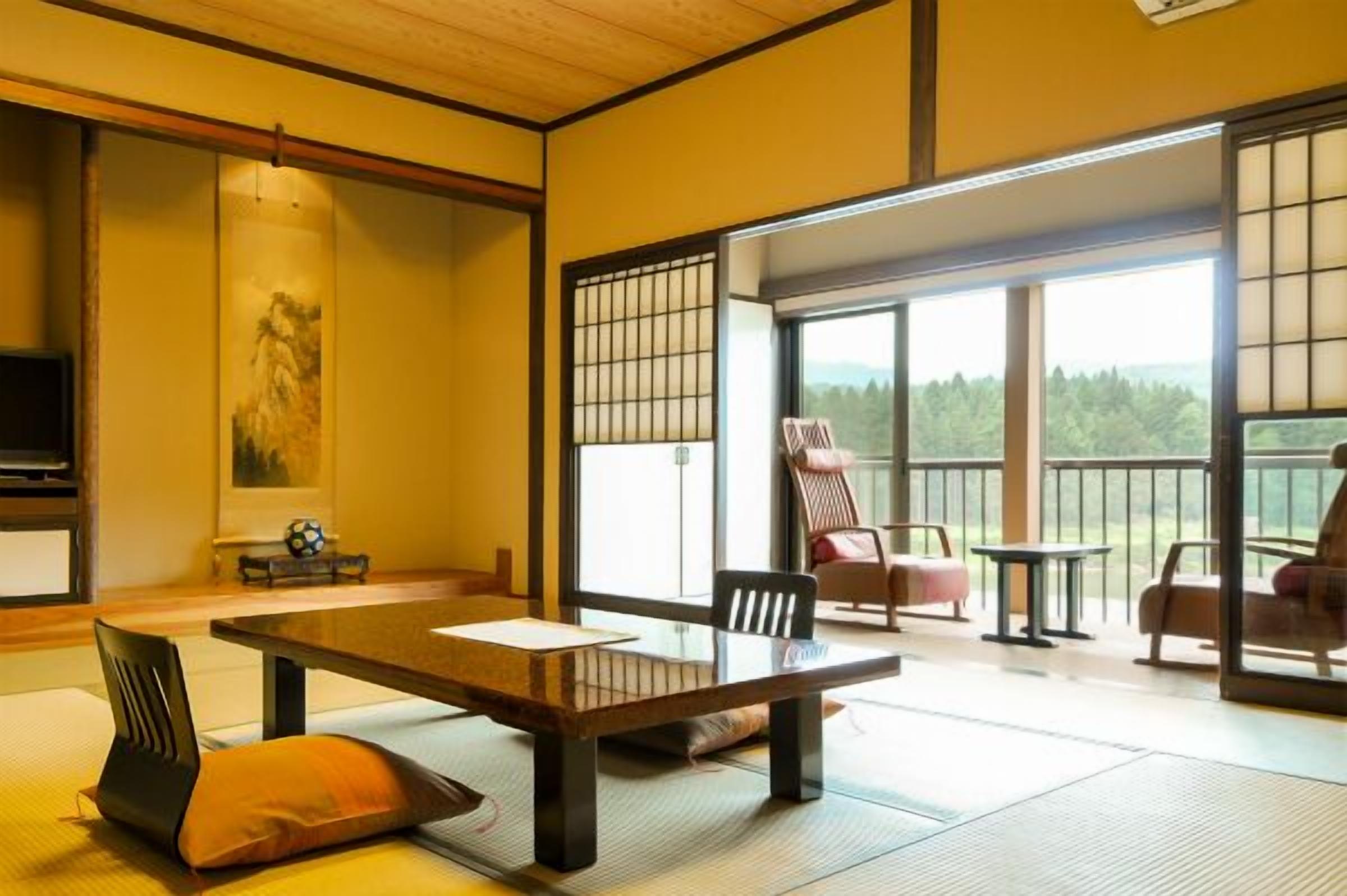 Une pièce de style japonais traditionnel, avec un sol recouvert de tatamis, une table basse, des chaises et une porte coulissante donnant sur un balcon avec vue sur la forêt.