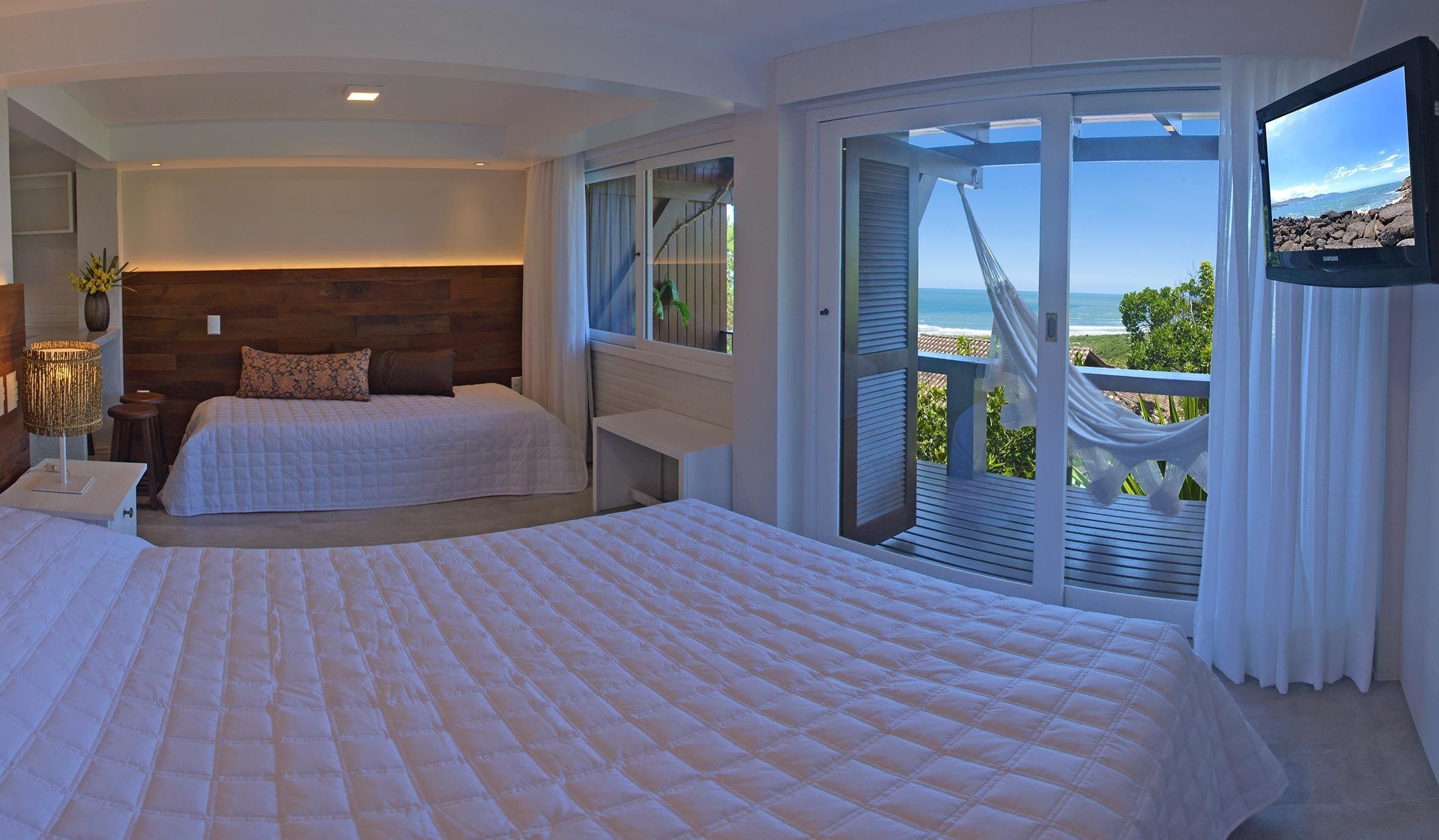 Ein Schlafzimmer mit zwei Betten, einem Fernseher und einem Balkon mit Meerblick.