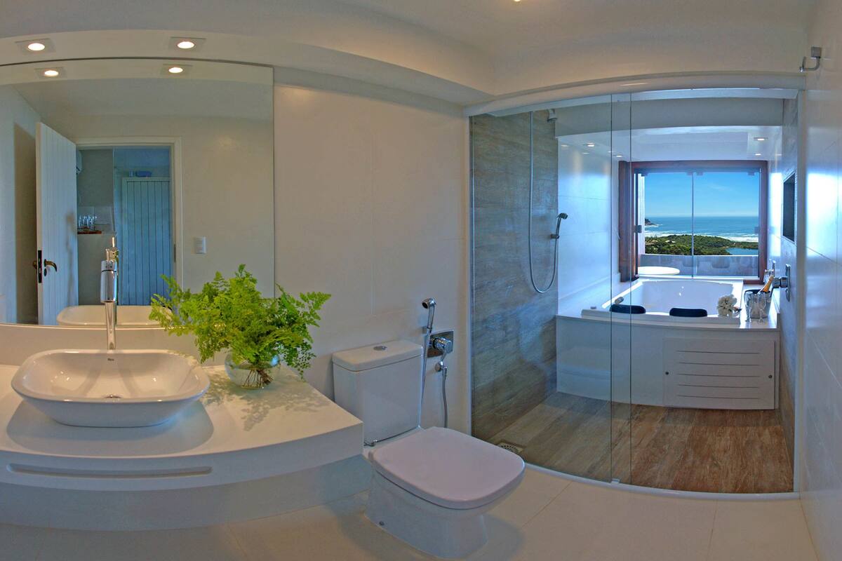 A modern bathroom with a large mirror, a sink, a toilet, and a shower area with a view of the ocean.