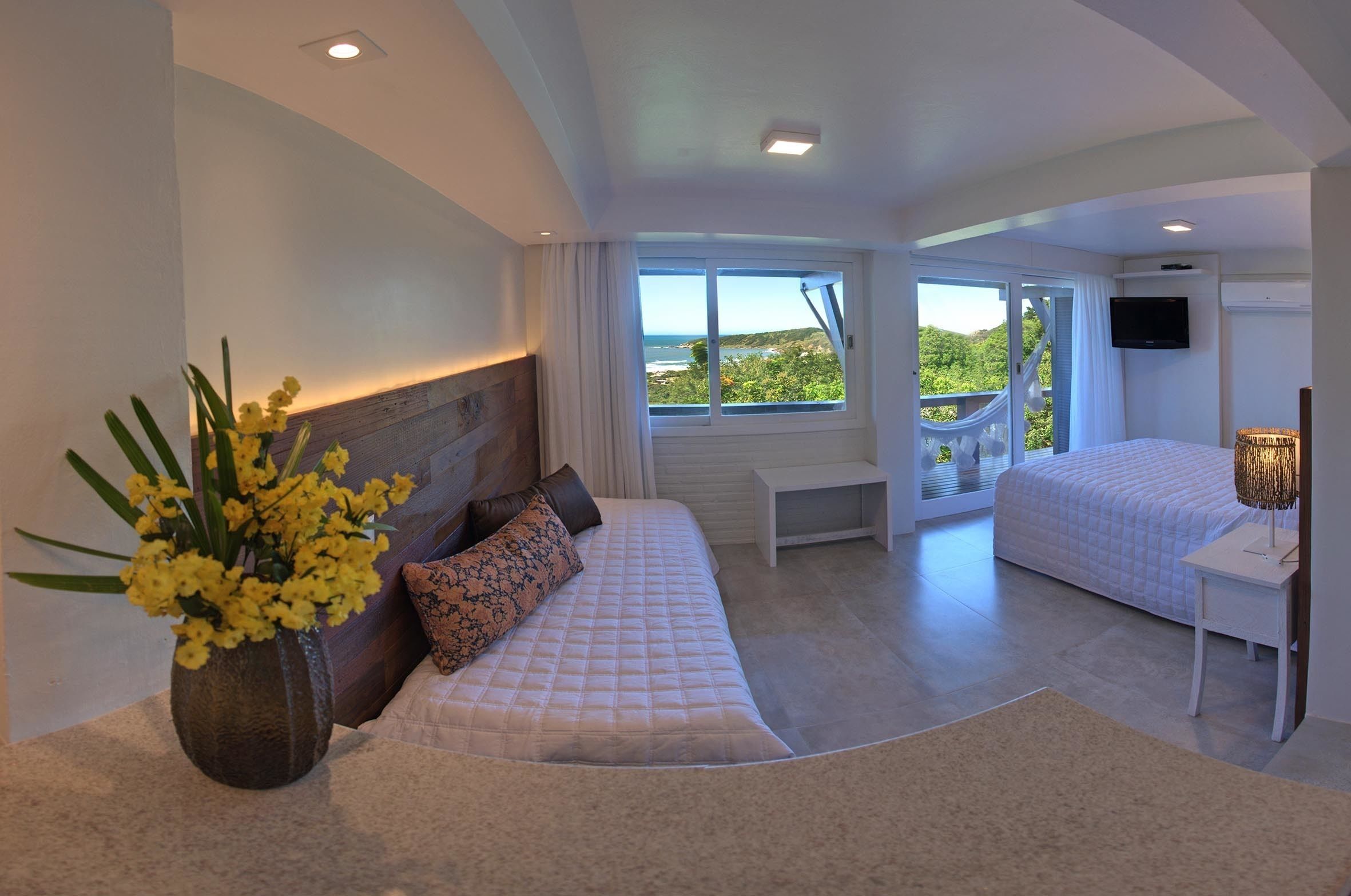 A bedroom with a large bed, a bedside table, a TV, and a window with a view.