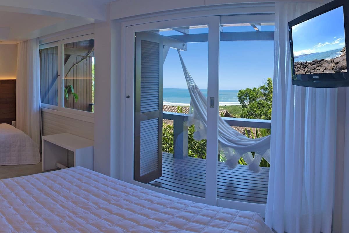 A bedroom with a large bed, a TV, and a balcony with a view of the ocean.