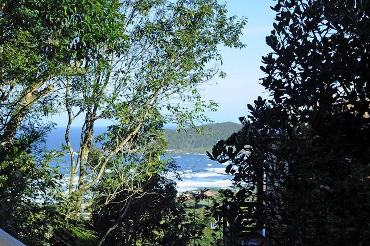 A hammock on a wooden deck overlooking a coastal view with trees and a clear sky.