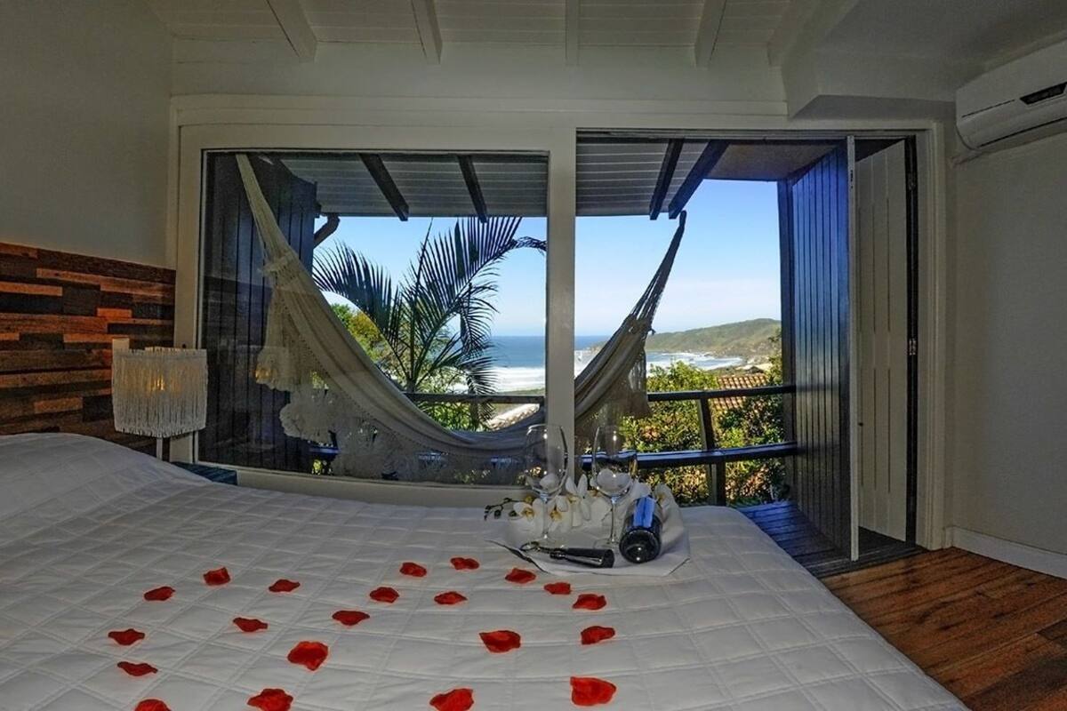 A bedroom with a large bed, a view of the ocean, and a hammock.