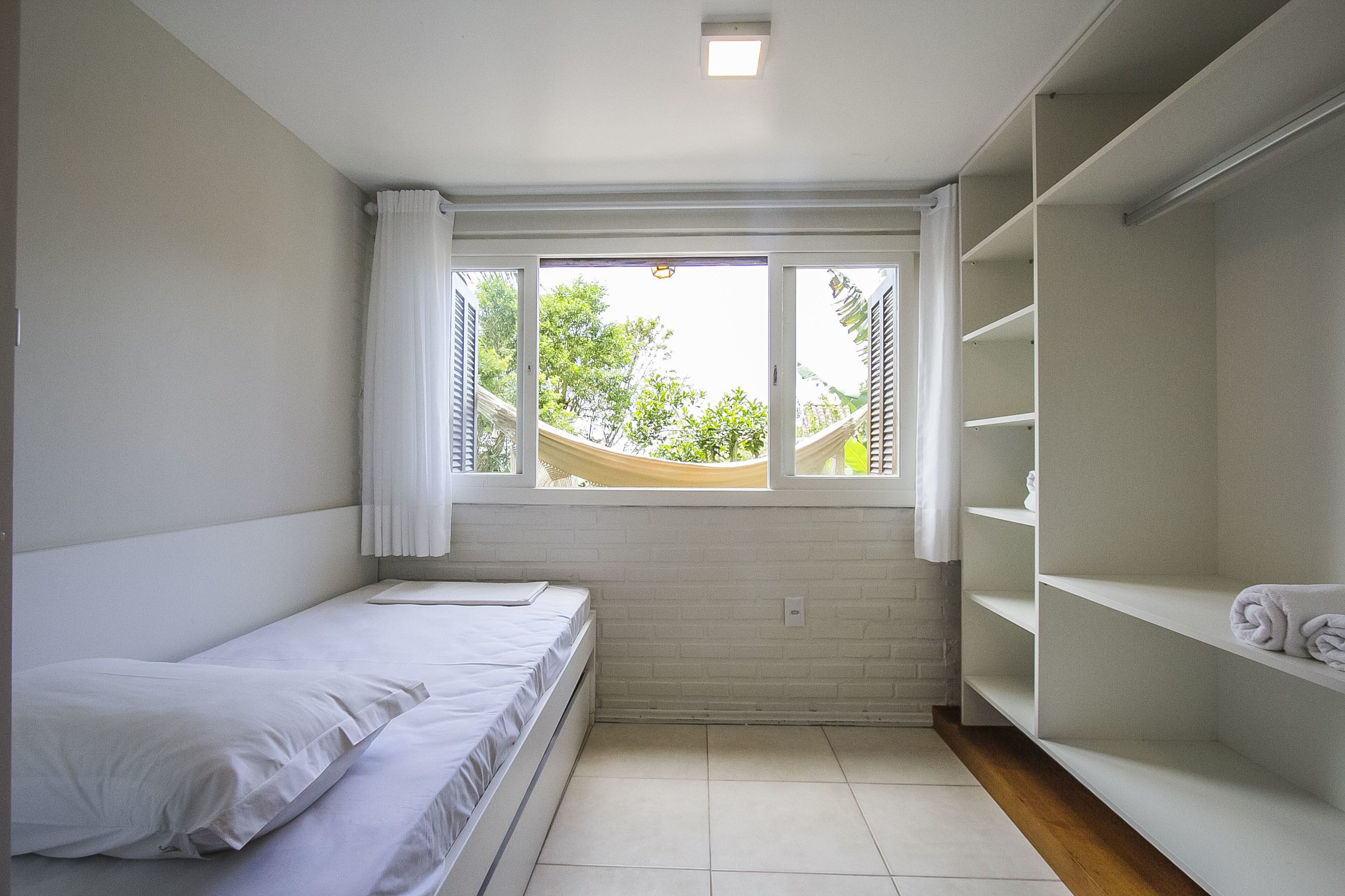 A small, bright room with a single bed, a window with a view of trees, and a built-in wardrobe.