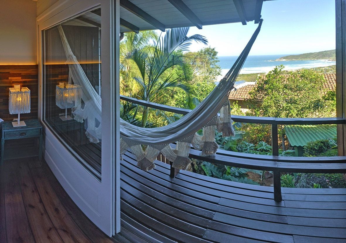 A balcony with a hammock, a wooden bench, and a view of the ocean and greenery.