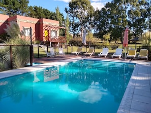 A swimming pool with sun loungers and a stone building in the background. - Icalma de la Sierra Apart Hotel Tandil (Tandil)