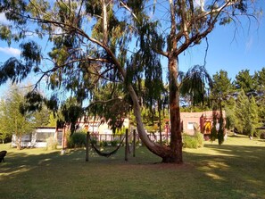 A large tree with a hammock in a grassy area, a building with a cross in the background, and a clear blue sky. - Icalma de la Sierra Apart Hotel Tandil (Tandil)