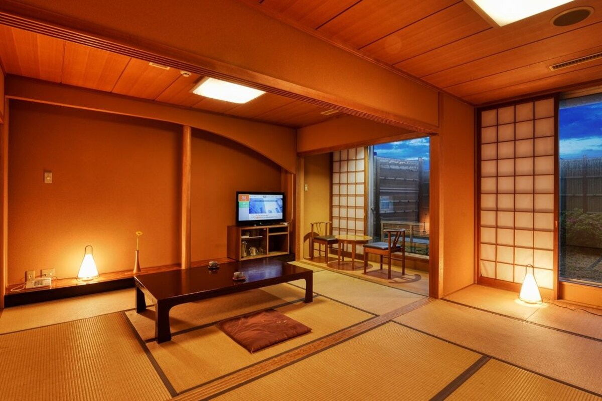 Une pièce de style japonais traditionnel, avec un sol recouvert de tatamis, une table basse, un téléviseur et des portes coulissantes donnant sur un balcon.