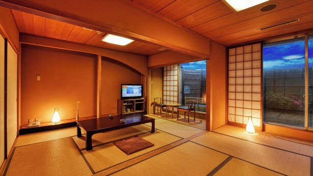 A traditional Japanese room with tatami flooring, a low table, a TV, and sliding doors leading to a balcony with a city view. - Plaza Hotel Mutsu (Mutsu)