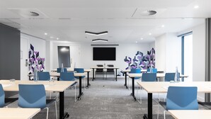 A conference room with a large screen, multiple tables with chairs, and abstract wall art.