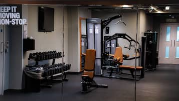 Un gimnasio con equipo de ejercicio, un televisor montado en la pared y un letrero que dice 'KEEP IT MOVING NON-STOP'.