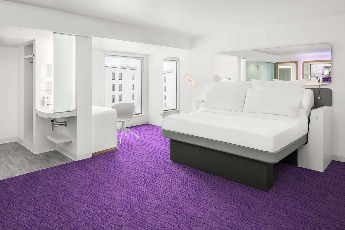 A modern hotel room with a large bed, a desk, and a chair.