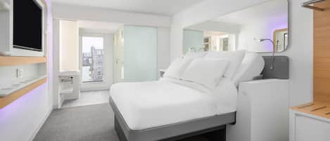 Habitación de hotel moderna con cama, televisor, espejo y vista a la ciudad.