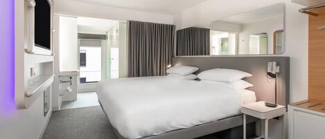 Una habitación de hotel moderna con una cama grande, mesitas de noche, un televisor y un espejo.