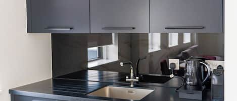 A modern kitchen with dark cabinetry, a stainless steel sink, and a kettle on the countertop.
