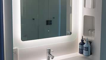 A bathroom with a large mirror, a sink, and a bottle of hand soap.