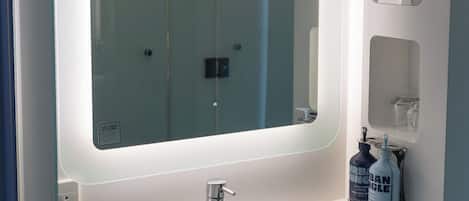 A bathroom with a large mirror, a sink, and a bottle of hand soap.